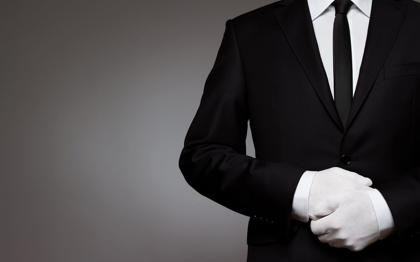 K2 chauffeur in a tailored dark suit holding open the rear door of an executive car in London